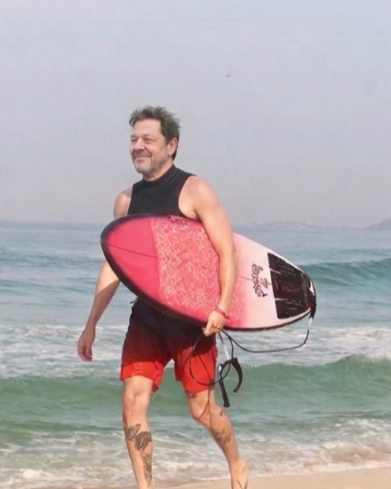 Serjão na praia carregando a prancha